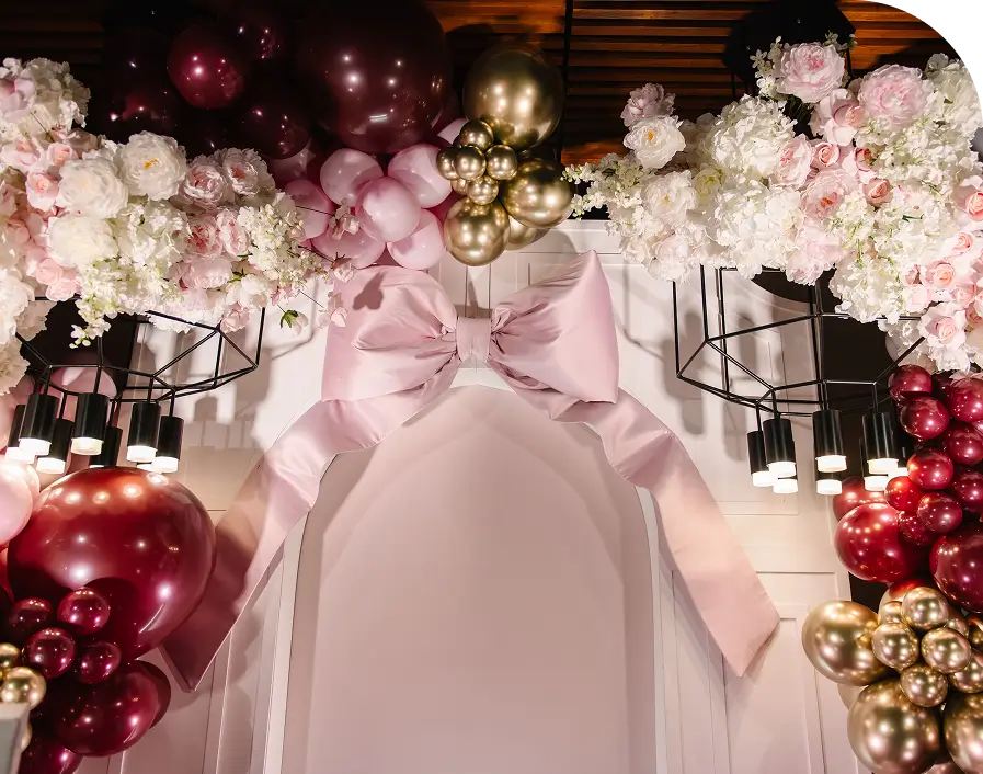 Floral arch with balloons and large bow.